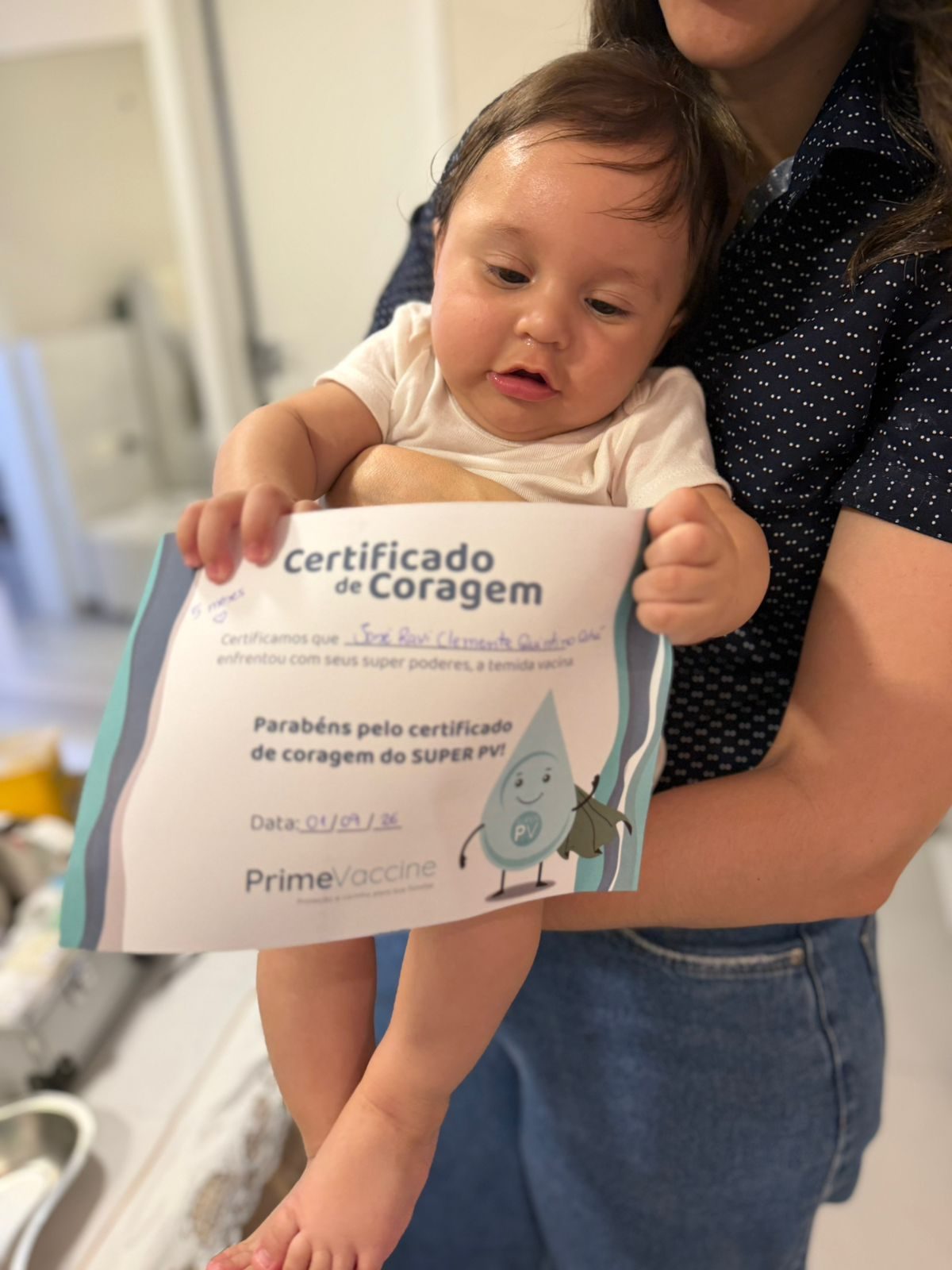 Bebê segurando o Certificado de Coragem do Super PV no colo da mãe