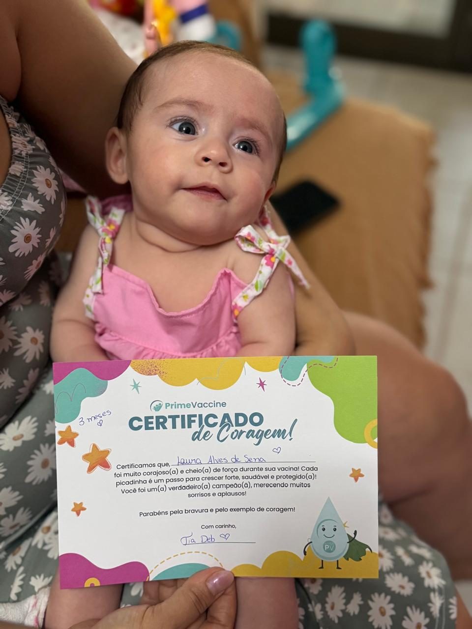 Bebê sorridente no colo da mãe com o Certificado de Coragem da Prime Vaccine