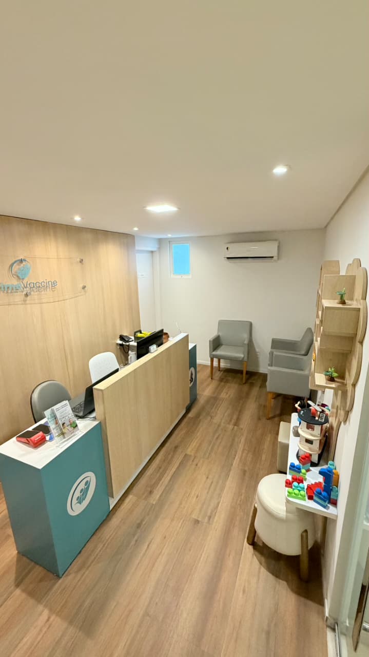 Recepção da unidade Graças da Prime Vaccine, com balcão em madeira, logo na parede e poltronas de espera