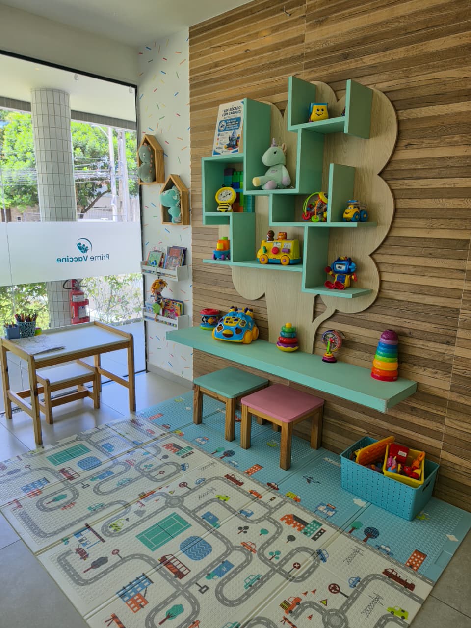 Brinquedoteca da unidade Poço da Panela com estante em formato de árvore, tapete de atividades e mesinha infantil