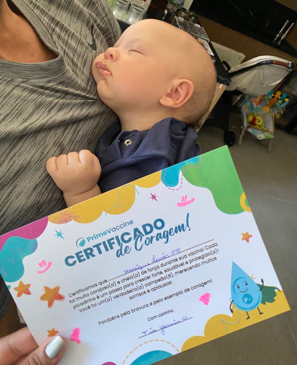 Bebê dormindo no colo da mãe segurando o Certificado de Coragem da Prime Vaccine