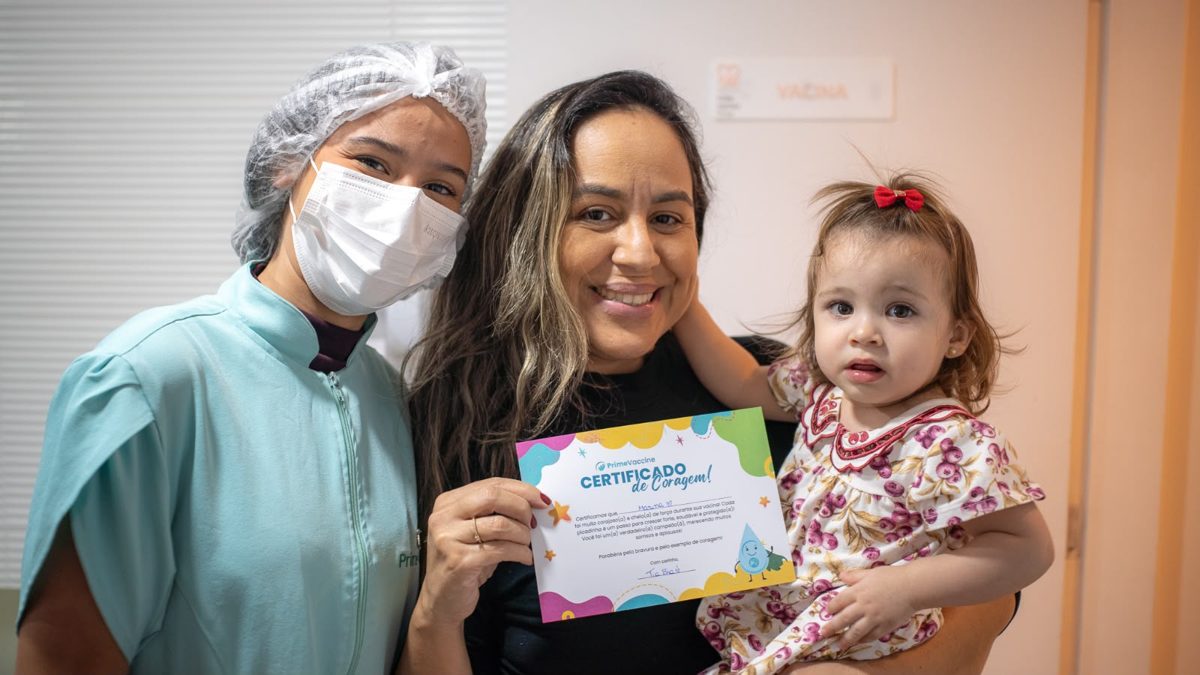 Mãe e filha com o Certificado de Coragem ao lado de profissional da Prime Vaccine
