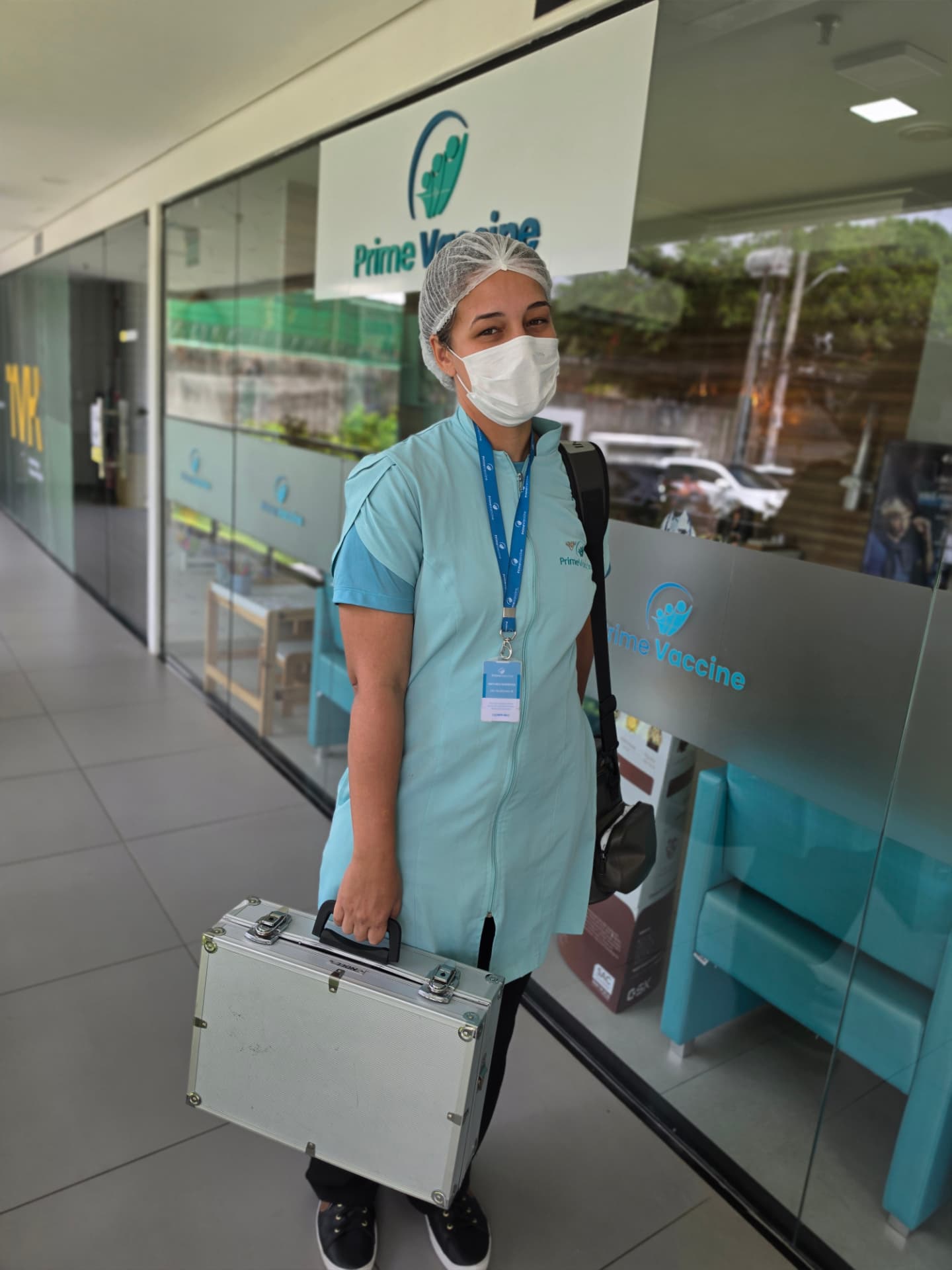 Profissional da equipe Prime Vaccine uniformizada, com identificação, carregando o equipamento térmico para atendimento domiciliar